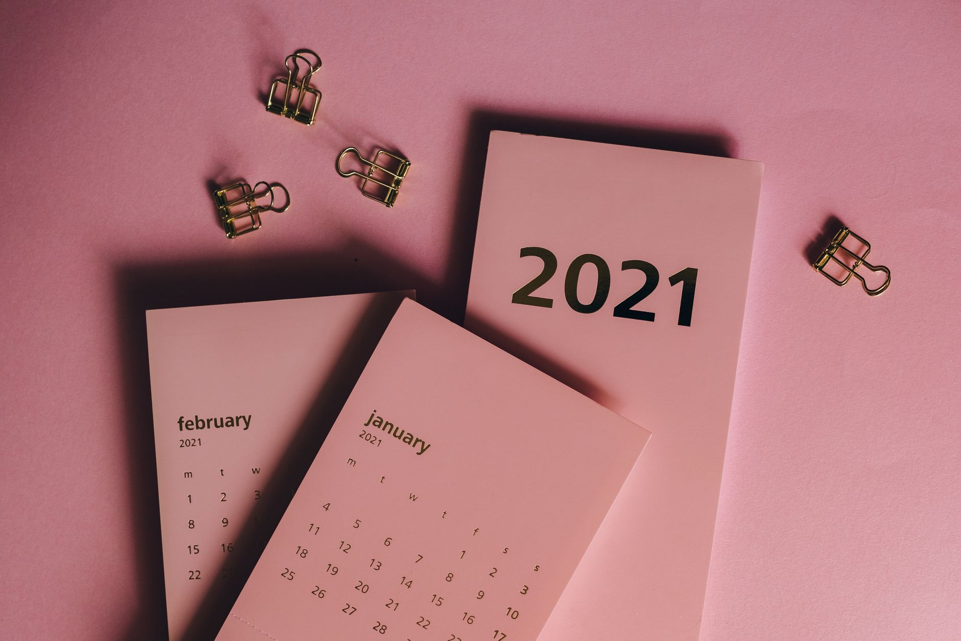 Top view of modern paper calendars with numbers and words near metal clips on pink background