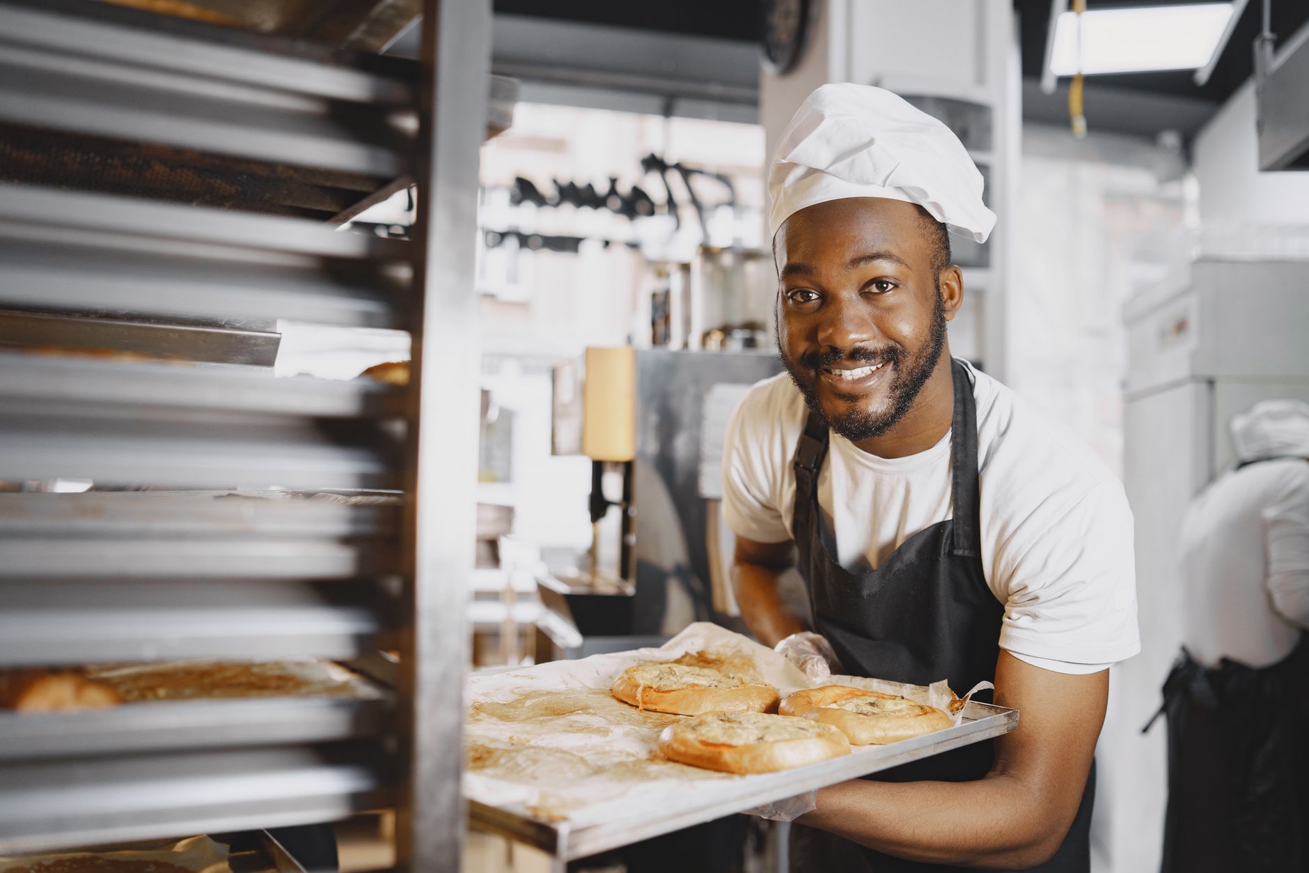 A cheerful baker presenting fresh breads from an industrial oven. Captured in a bakery setting.