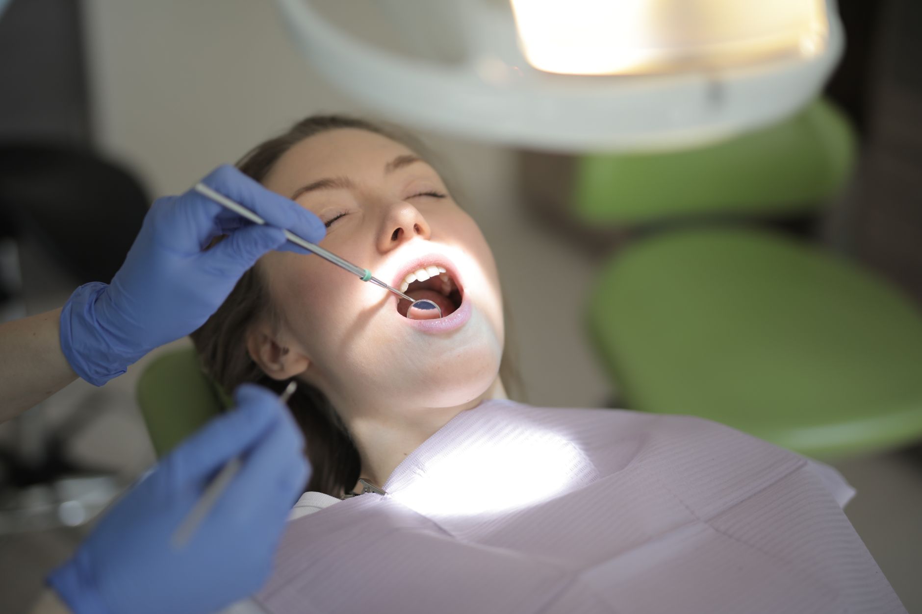 From above view of crop unrecognizable dentist in latex gloves using medical instruments while examining teeth of patien