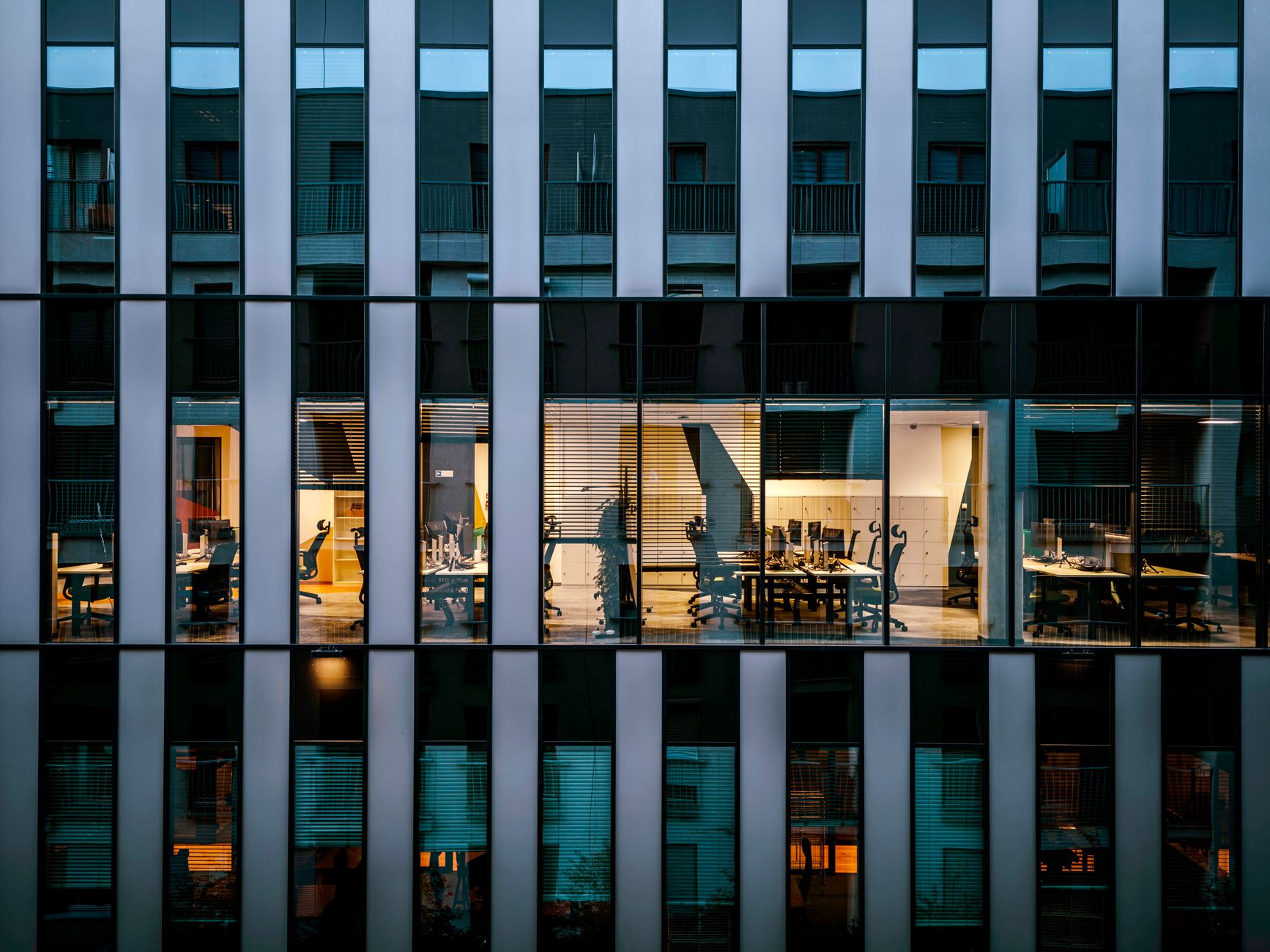 Illuminated office inside a modern glass building exterior, showcasing architecture and workspace design.