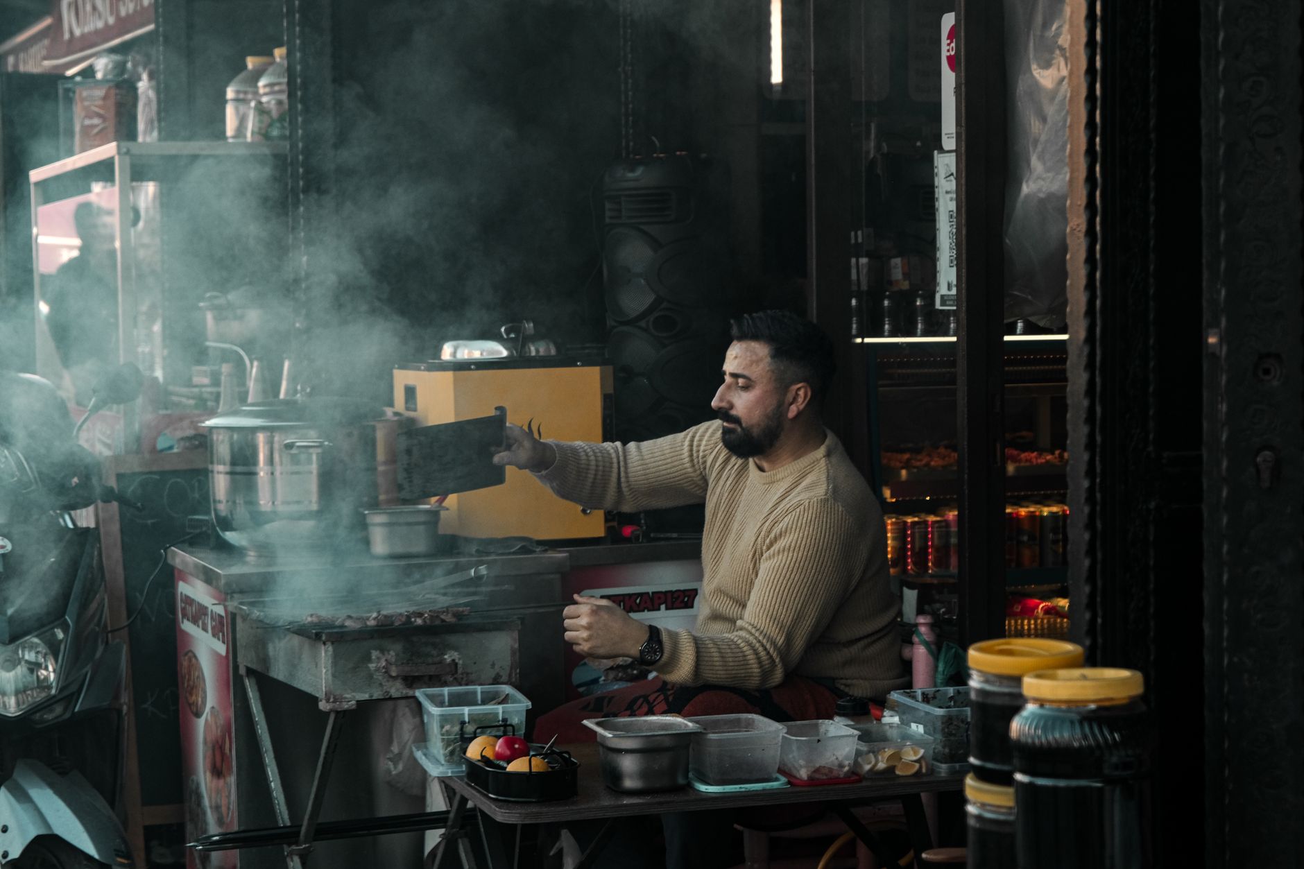 A street vendor prepares food amidst smoke, creating a moody urban scene.