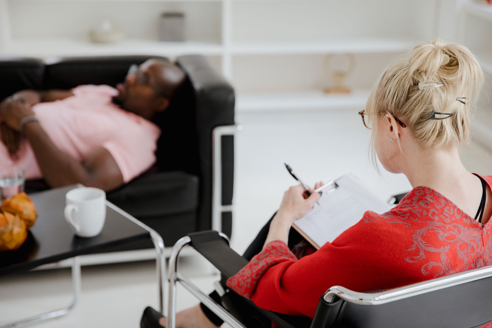 A professional therapist takes notes during a therapy session, engaging with a client.