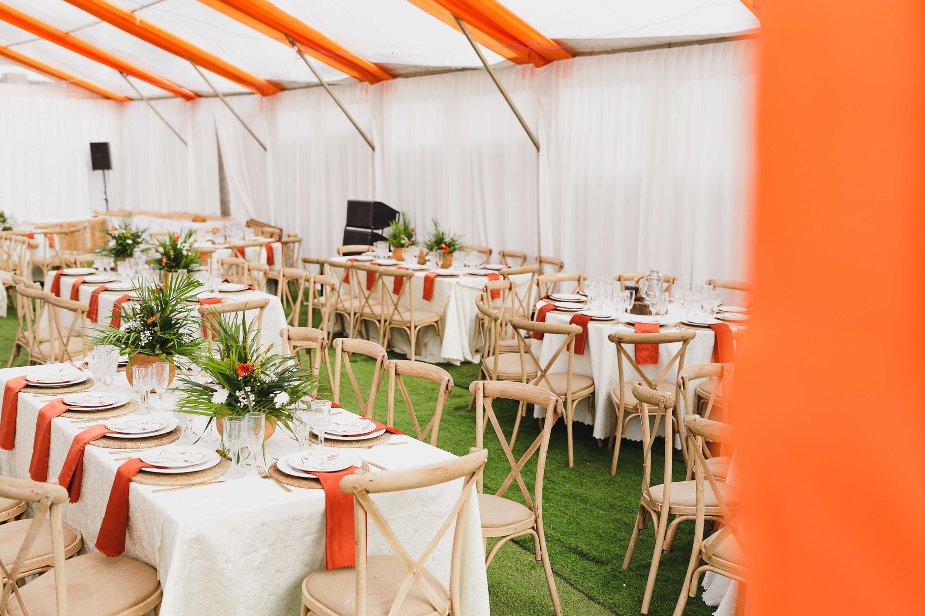 Beautifully arranged event tables with floral centerpieces inside a white and orange tent.