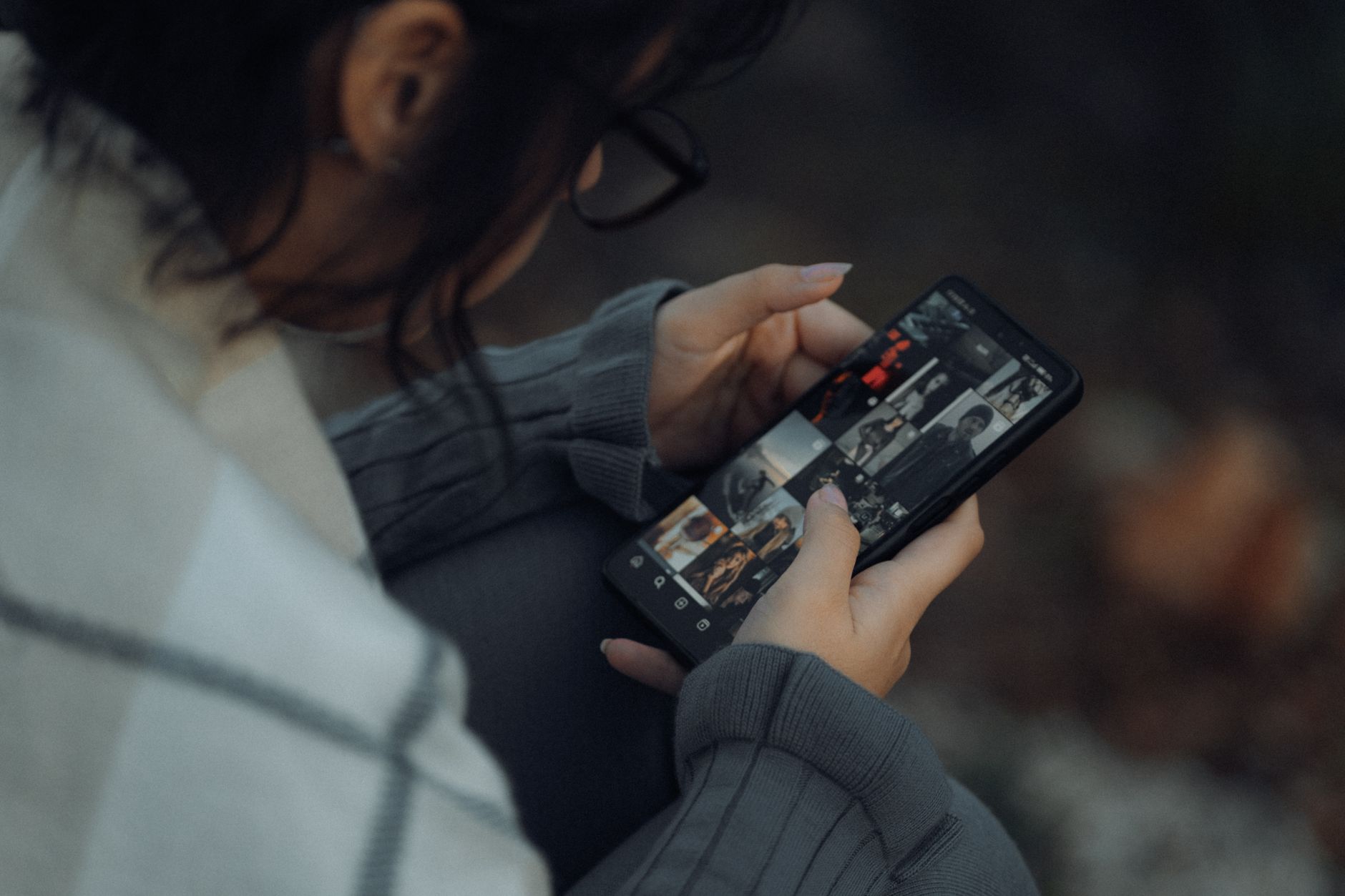 Young woman browsing photo gallery on smartphone outdoors, showcasing technology and lifestyle.