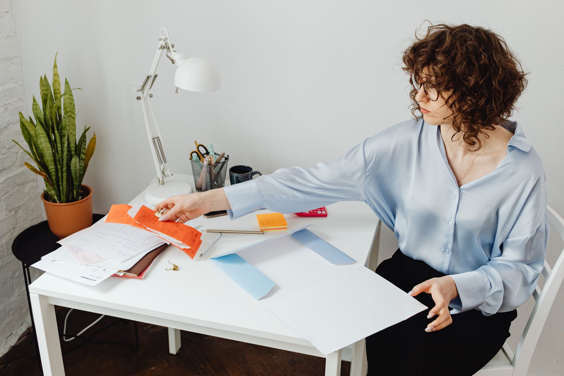 A woman organizing papers at her desk, working in a bright office environment.