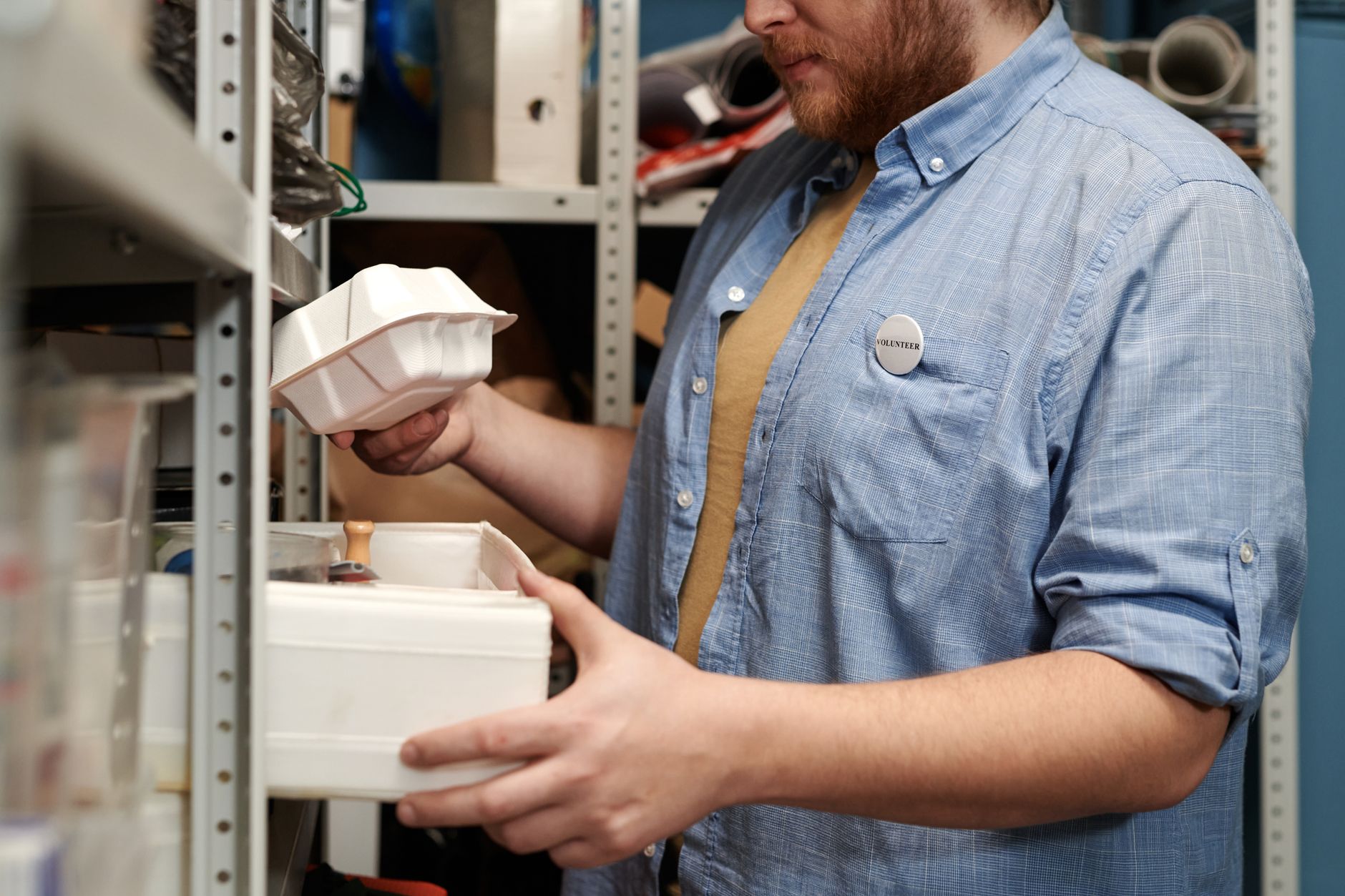 A male volunteer organizing supplies in a cluttered storeroom.
