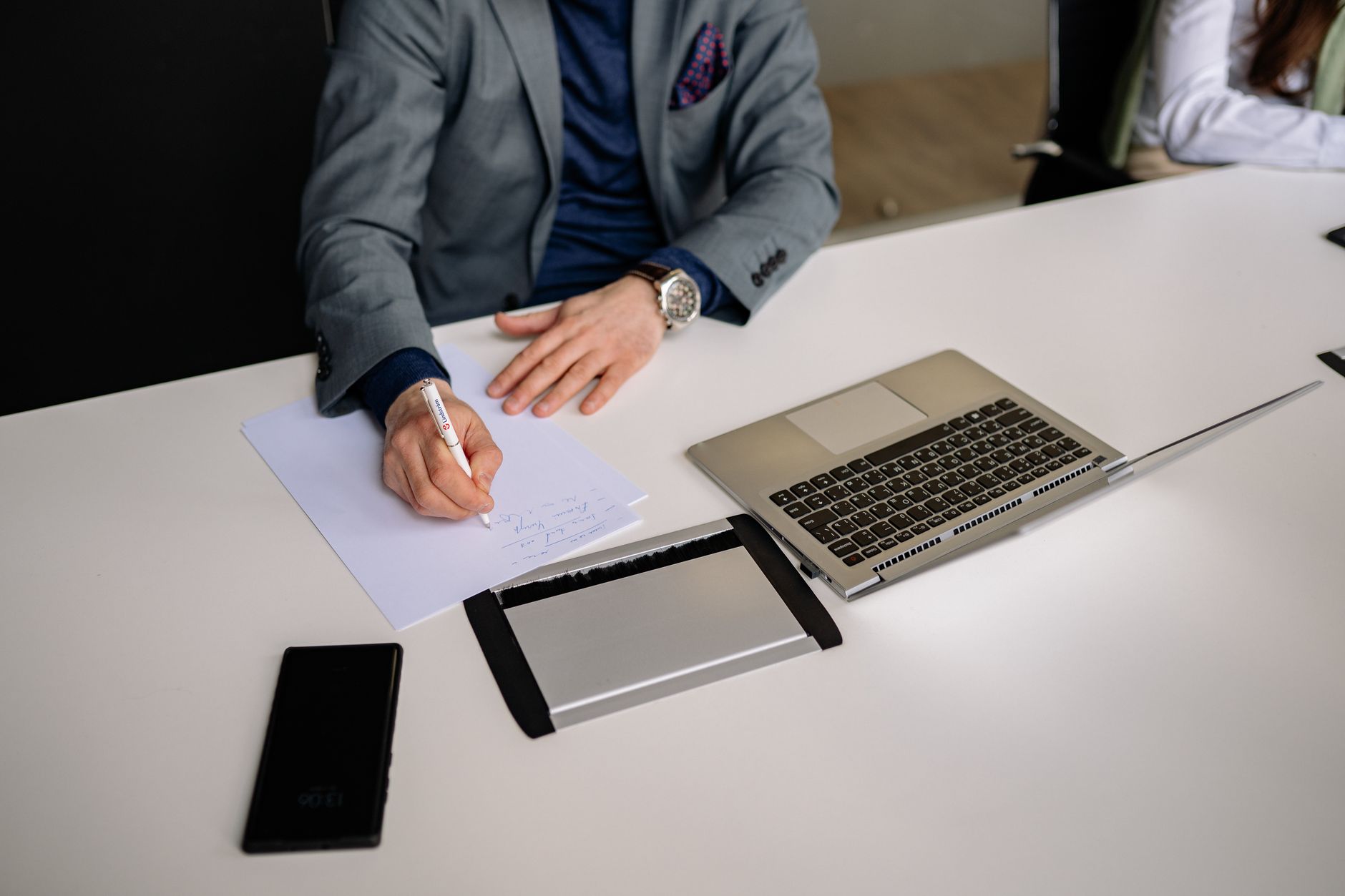 Professional businessman writing notes in a modern office environment with laptop and smartphone.