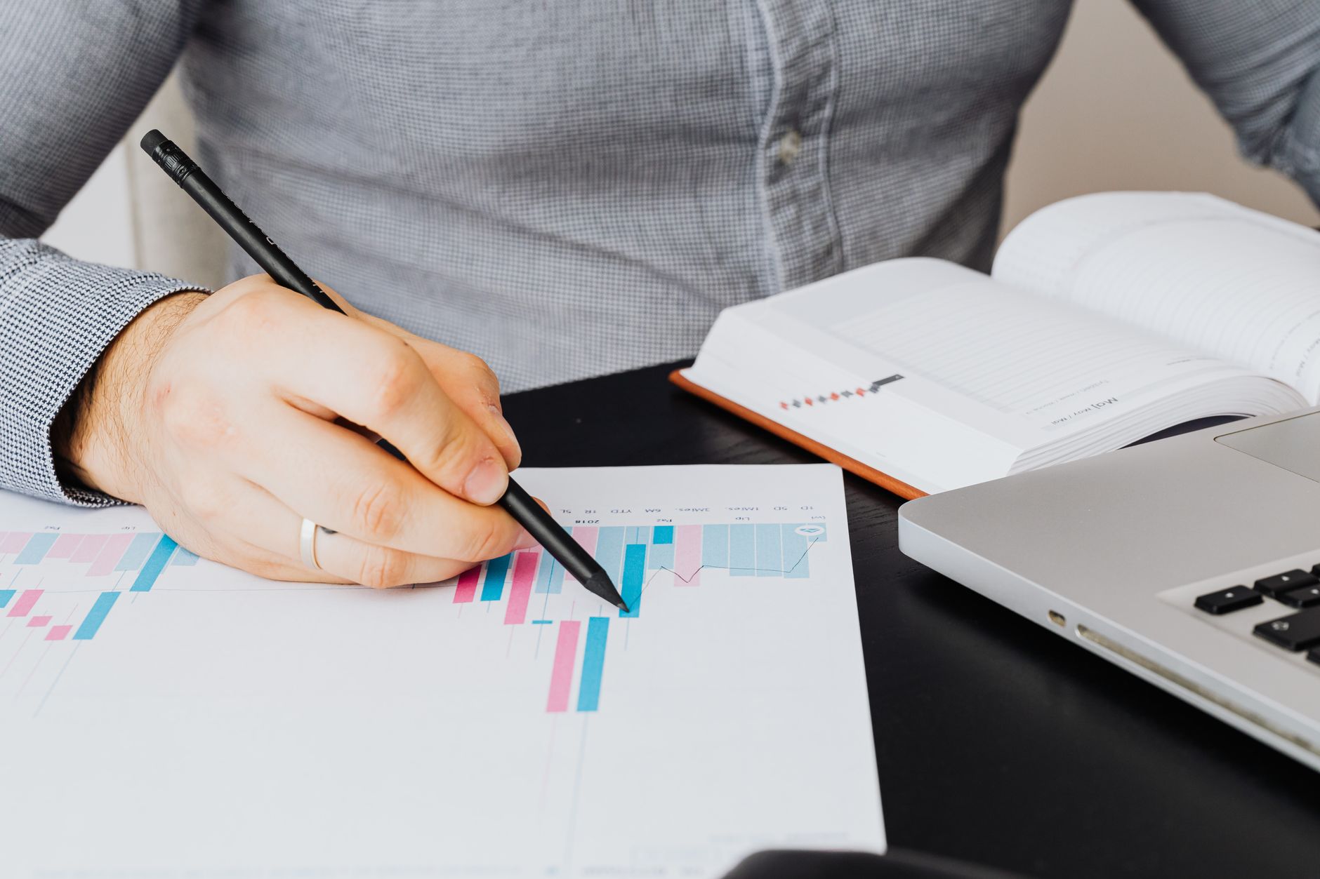 A business analyst examines a graph on paper with a laptop and notebook indoors.