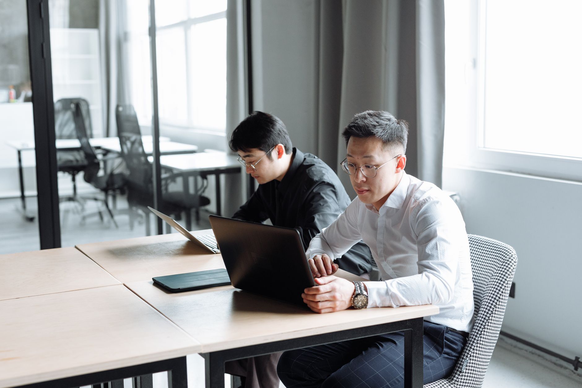 Two men working intently on laptops in a bright, modern office setting.