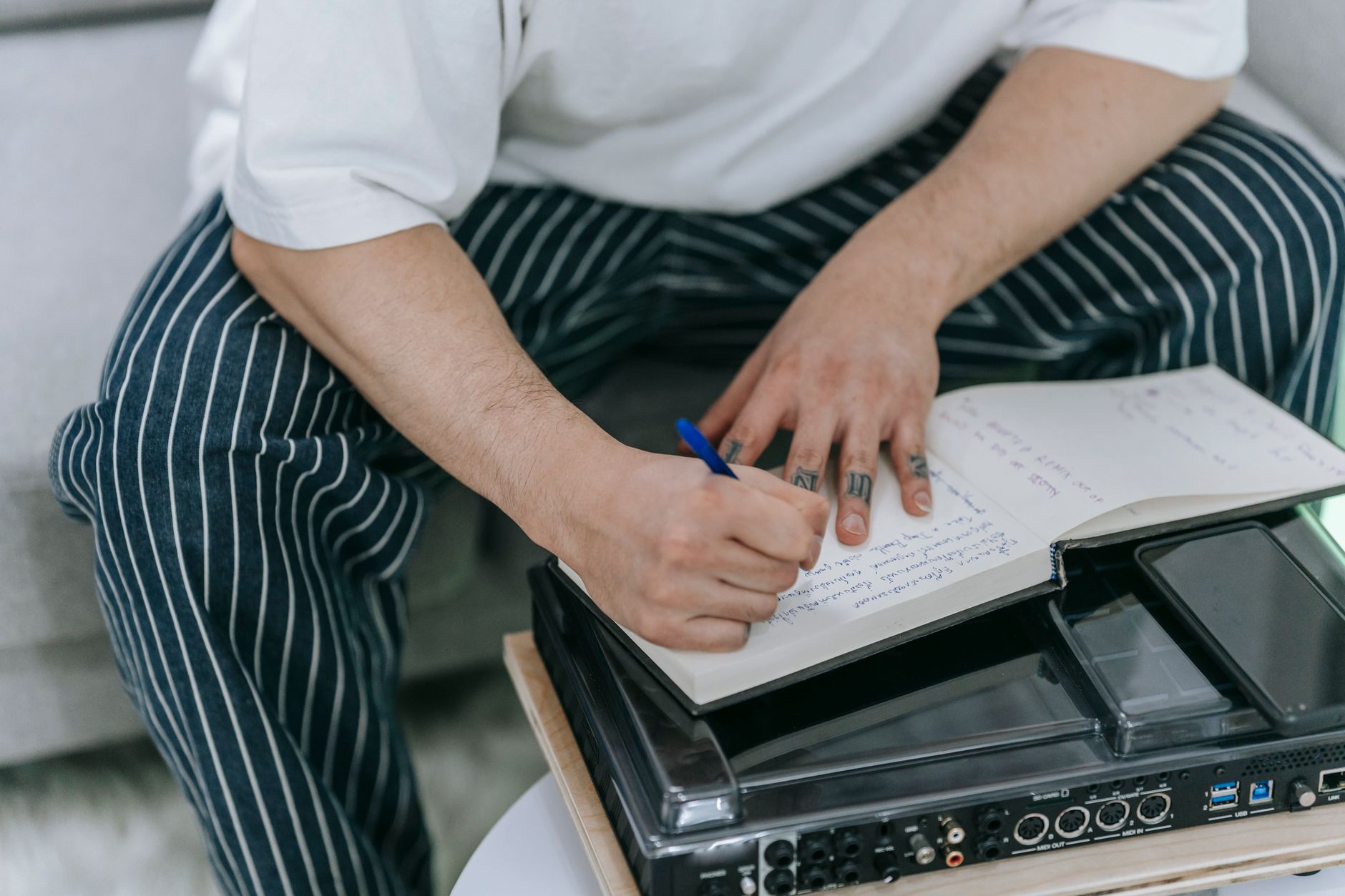 Tattooed individual writing in a notebook indoors, focusing on creativity and expression.